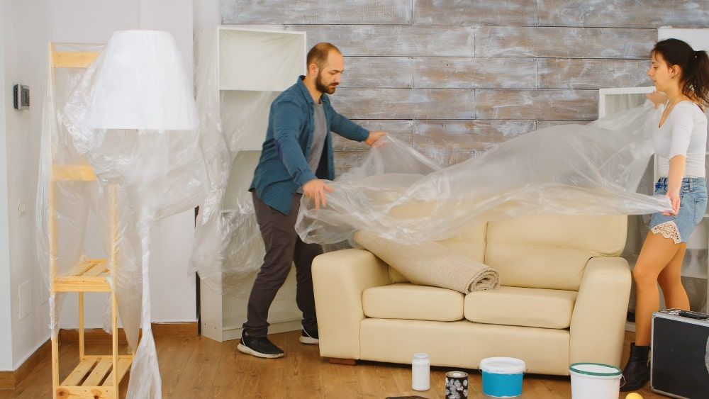 couple-wrapping-sofa-plastic-foil-protection-while-they-are-renovate-living-room-home-renovation-construction-painting-work-min.jpg