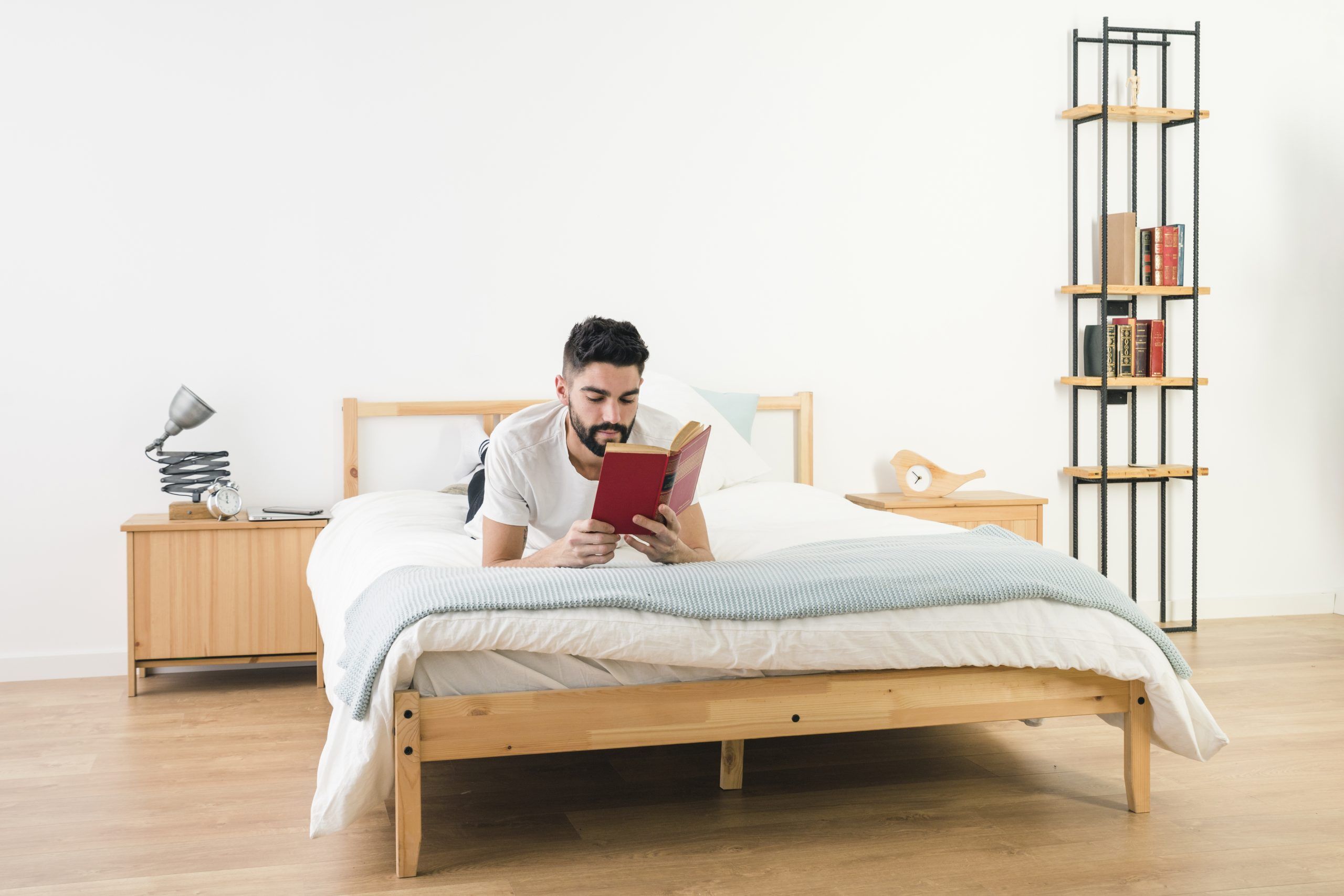 A man lying on a bed in a cozy bedroom, reading a book and enjoying a relaxing moment